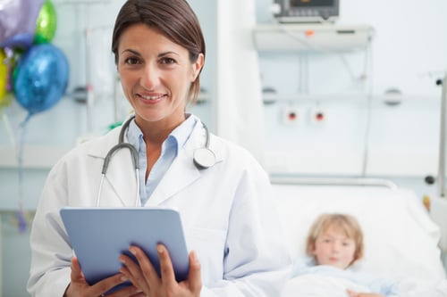 Female doctor holding a tablet computer next to a child in hospital ward